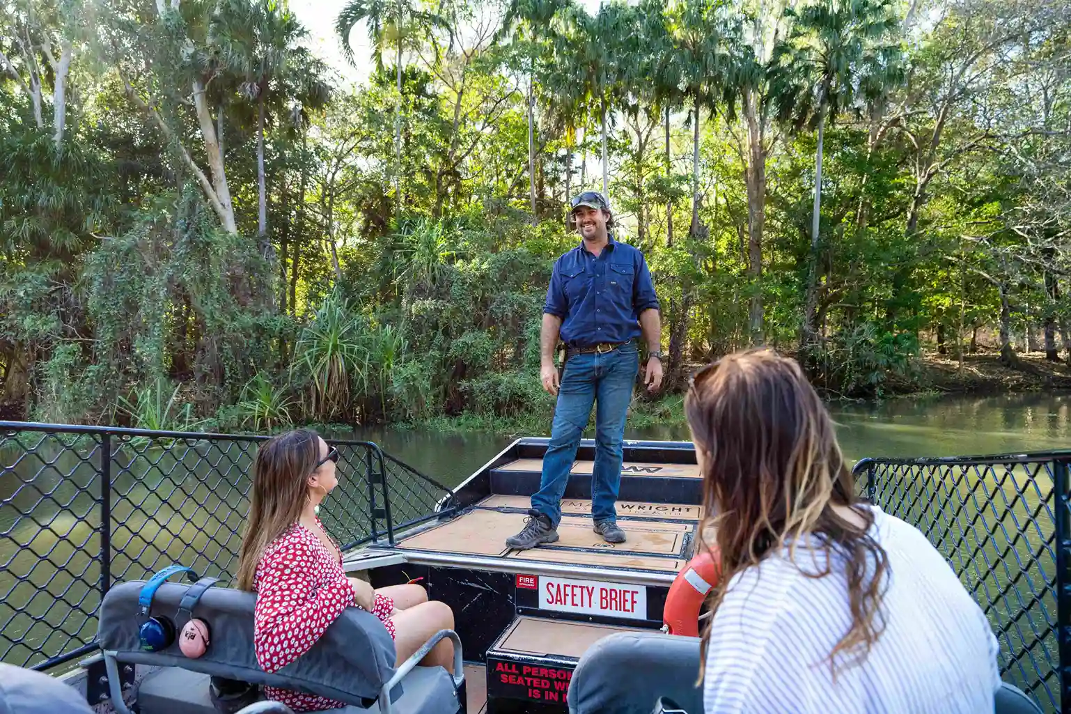 Tour guide giving a safety briefing to visitors on an airboat before a wildlife tour through tropical wetlands in Australia.