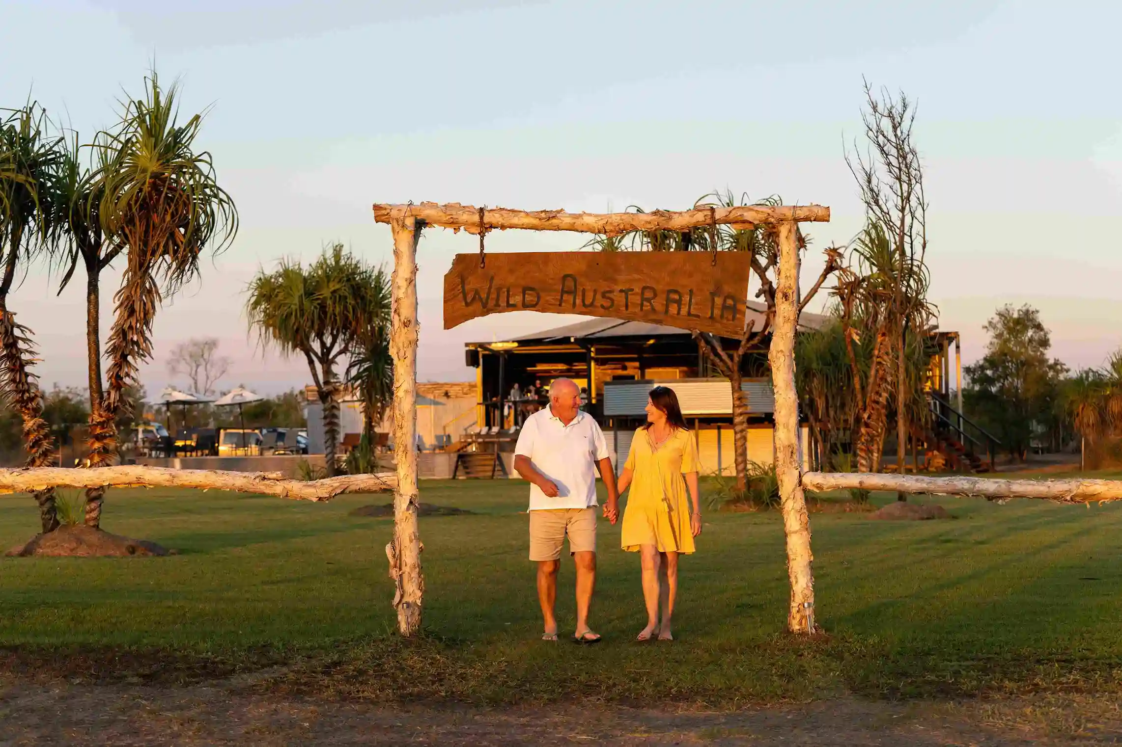 Couple walking under the Wild Australia entrance sign at an outback tourism lodge during sunset.